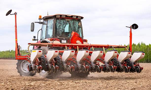 istock Precision inline seeder. A row seeder. Seed drill. Tractor with mounted seeder performing direct seeding of crops on plowed agricultural field. Farmer is using farming machinery for planting process. 2216054396