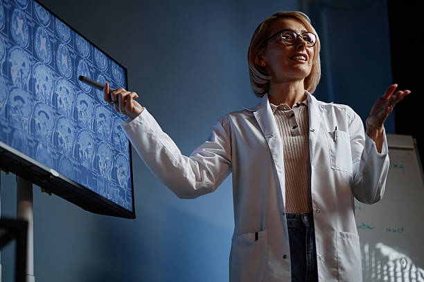 istock Female Physician Presenting Lecture Pointing at Screen with Brain MRI in Clinic 2216054746
