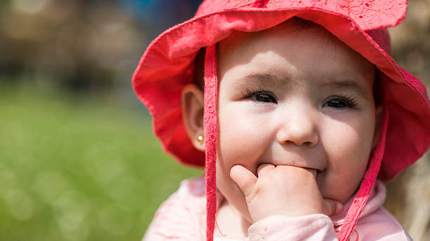 A close-up shot of a mother and daughter sitting together on a beach in Seaton Sluice. The daughter is lying on her mother's legs while the mother feeds her berries. The daughter is wearing a pink sun hat to protect her from burning.Videos are available similar to this scenario.