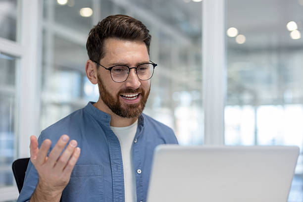 istock A man in glasses and a blue shirt is smiling while on a video call using his laptop. 2216059444