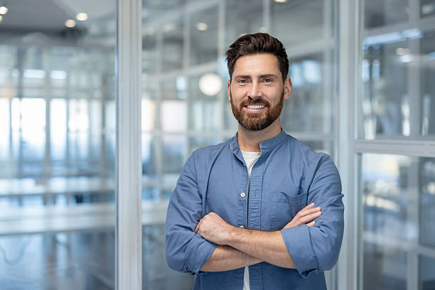 istock A confident, smiling businessman stands with crossed arms in an office setting. 2216059481