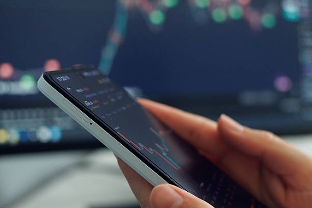 istock User interacts with stock market data displayed on a smartphone, with market analytics visible on a computer screen in the background 2216061963