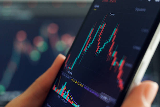 istock A person analyzes stock trends on a smartphone, studying candlestick charts and trading data, with market indicators blurred behind 2216061972