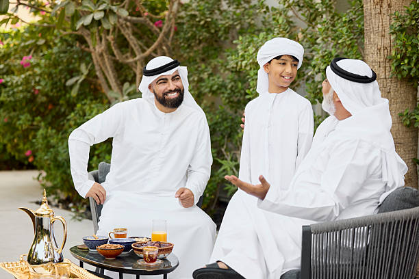 Grandfather talking with boy while sitting on chair in back yard. Happy middle eastern family is spending leisure time. Snacks and refreshments are arranged on table.