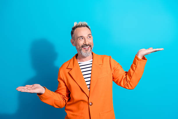 istock Smiling mature man in stylish orange jacket making friendly gestures with hands against bright blue background 2216063287