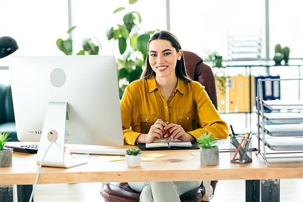 istock Professional brunette female worker in a modern office smiling and working at her desk with computer during a productive work day. 2216065670
