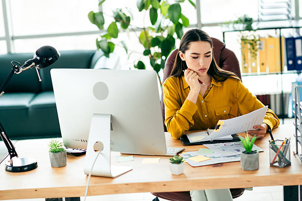 istock Young professional woman analyzing documents at her modern office desk with a computer and organized layout in a bright workspace 2216065671