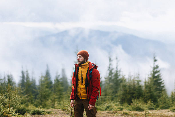 The confident handsome man standing proudly at the misty mountains background in springtime