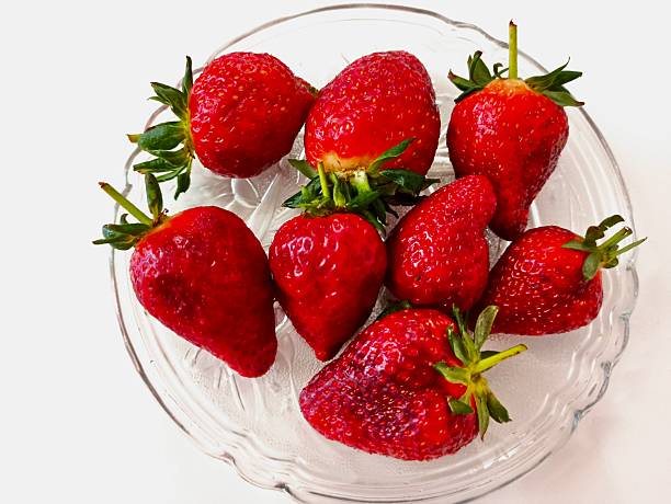 Strawberries on clear glass plate over white background, fresh berries, summer fruit, healthy snack, minimal composition, vibrant red color, clean food photography, natural dessert, top view.