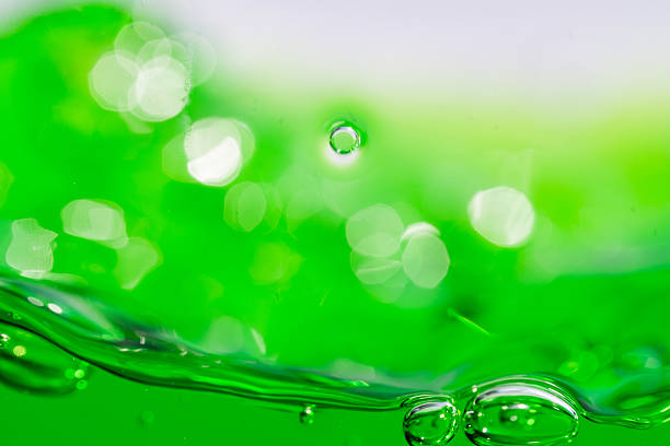 198.Two air bubbles partially submerged in green liquid. White background and reflections highlight fluid tension, bubble shape, and surface clarity.