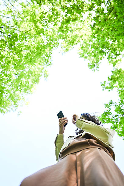 istock Young woman using smartphone under green trees canopy 2216070306