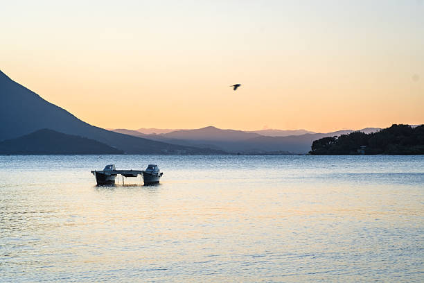 Empty catamaran stopped in calm waters, on a sunny day, with mountains in the background and a peaceful atmosphere