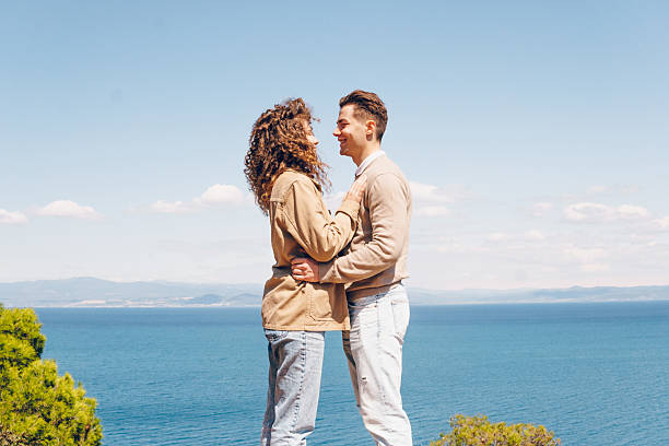 Happy couple standing and kissing on the beach. They enjoy in beauty spring day on the sea.