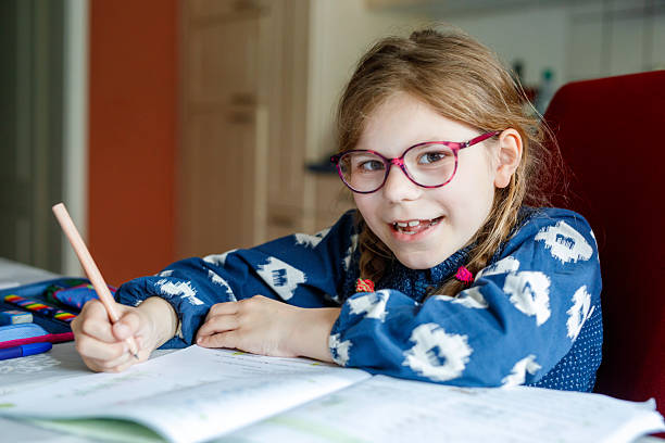 istock Cute elementary school girl sitting at a desk at home, writing in her workbook and doing school homework. Focused child learning and studying indoors. Concept of education, childhood, home learning. 2216078462