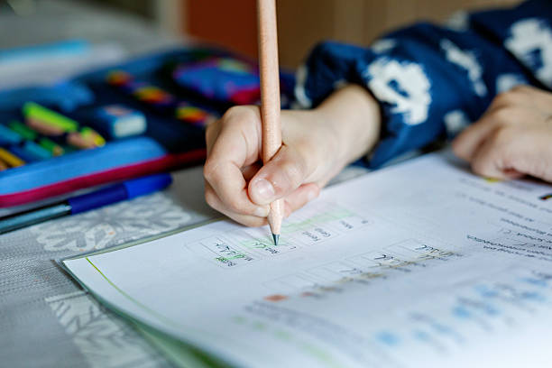 istock Cute elementary school girl sitting at a desk at home, writing in her workbook and doing school homework. Focused child learning and studying indoors. Concept of education, childhood, home learning. 2216078476