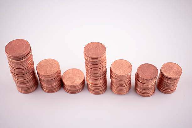 Stacks of coins, predominantly copper-colored with some gold and silver tones. Various heights suggest denominations of differing values. Coins are neatly arranged against a neutral background, indicating themes of savings, investment, or financial management. The metallic texture and circular shapes are evident, highlighting concepts of currency and economy.
