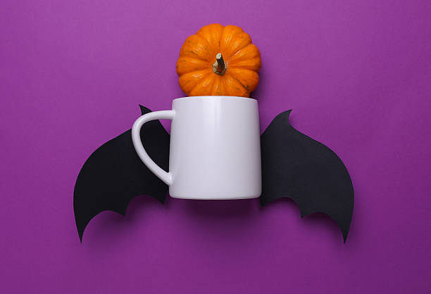 istock White ceramic cup mockup for your design and Halloween decorative bat wings and pumpkin on purple background 2216085269