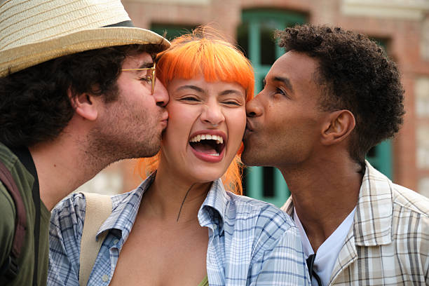 Two friends are kissing a girl on her cheeks while she is laughing, showing a playful and affectionate moment