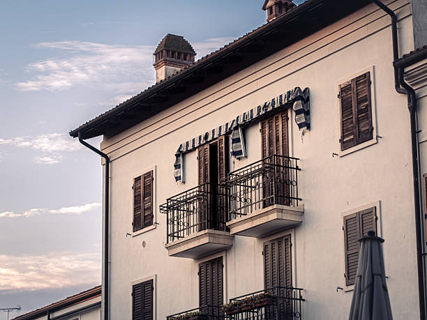 Elegant cream-colored facade with wooden shutters and twin balconies under striped awnings, captured in the warm evening light in Grado, Italy.