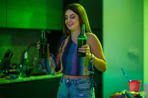istock Smiling Young Woman at a Gathering Holding Beverage Bottles in a Vibrant Setting 2216088692