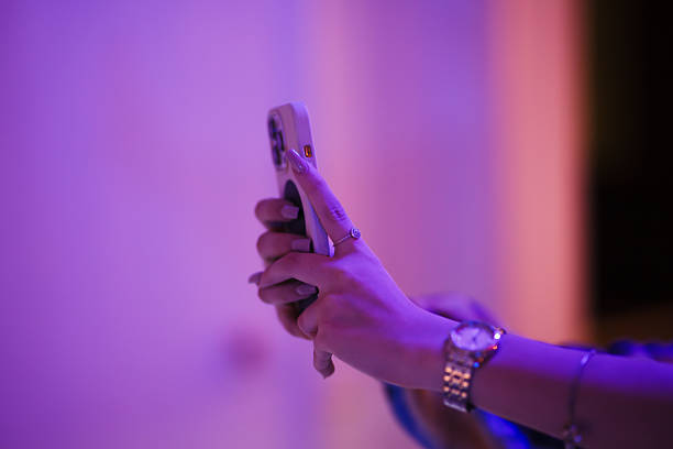 istock Closeup of a person texting using a mobile phone in an illuminated purple setting 2216088719