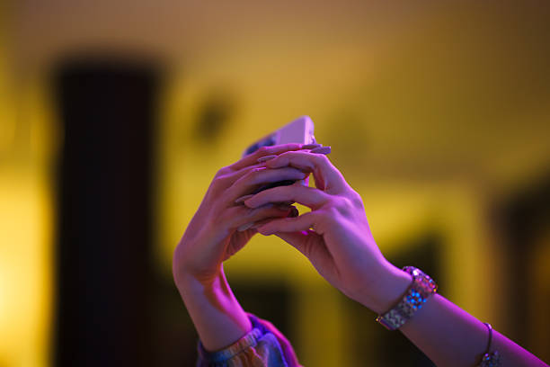 Hands photographed holding a smartphone amid a blurred, colorfully lit background, evoking modern technology, communication, and nightlife themes with a focused perspective.