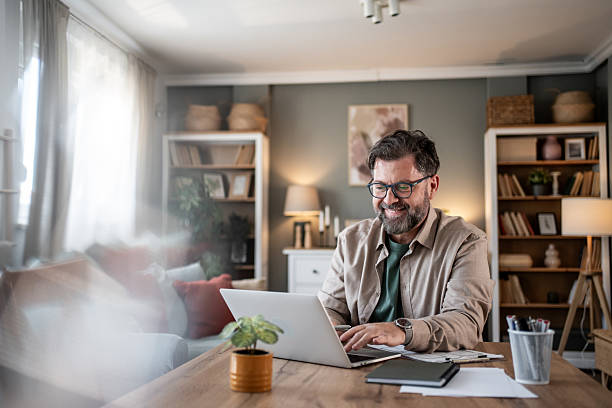 Smiling mature man working remotely from home office using laptop