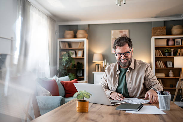 istock Mid adult man working from home sitting at dining table checking paperwork and smiling 2216091911