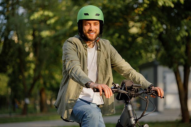 istock Smiling man rides bicycle wearing helmet in park during sunny day 2216095510