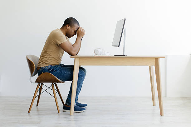 istock Stressed African American man sitting at desk with head in hands 2216095768
