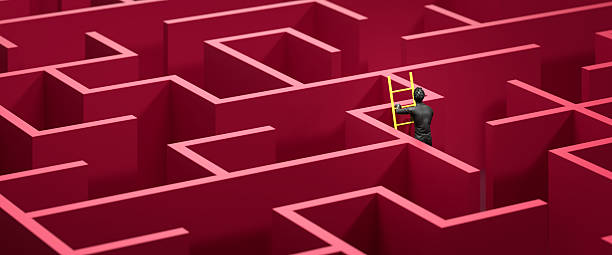 istock Concept - solving a complex problem by thinking out of the box or cheating. Dark red maze and floor with a yellow ladder against the wall and a black figure climbing the ladder. Web banner format 2216097925