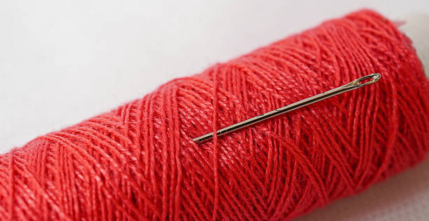 istock A spool of Red sewing thread with a needle next to it isolated on a white background. Selective focus. Abstract Images. 2216101618
