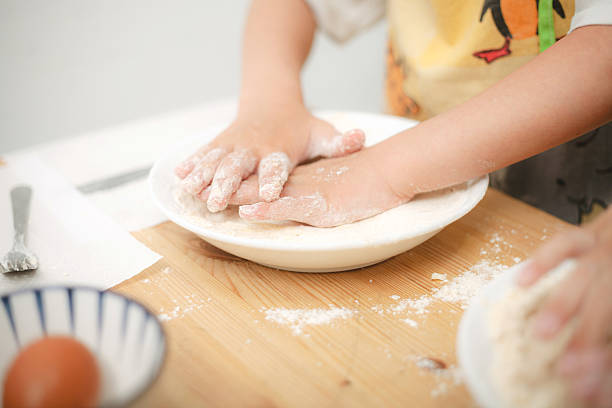 Child's hands kneading cookie dough in bowl on wooden table