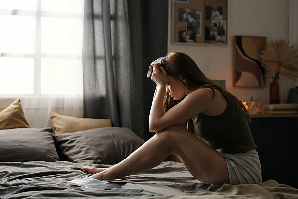 istock Contemplating Woman Sitting on Bed in Dimly Lit Room 2216111455