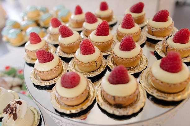 Elegant Italian dessert tartlets with vanilla custard and fresh raspberries displayed on a mirrored tray.