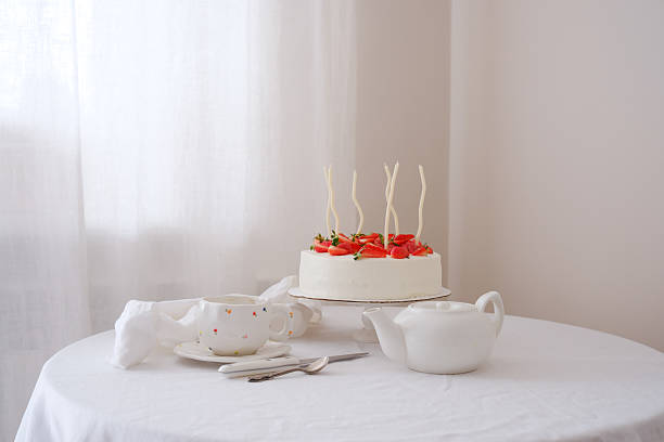 A small birthday cake with a beautiful string of silver candles on a wooden table with a glass background and green trees as a background.