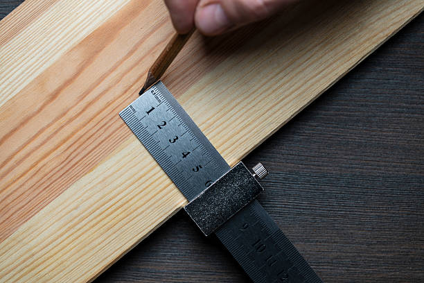 istock Carpenter steel ruler with limit block for marking or template, closeup, top view. The worker hand holds a metal ruler and marks on a wooden board with a pencil 2216119084