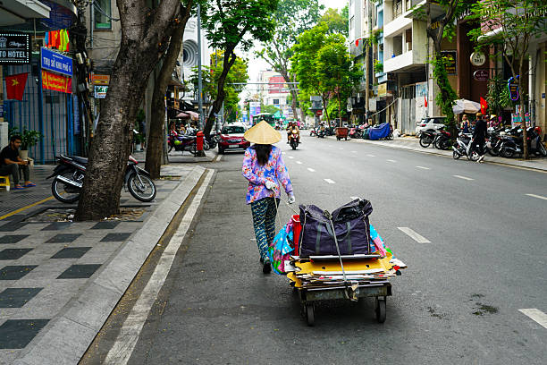 Hanoi, Vietnam - November  20, 2022: Street vendor carrying transporting goods in baskets using a carrying pole, also called a shoulder pole.