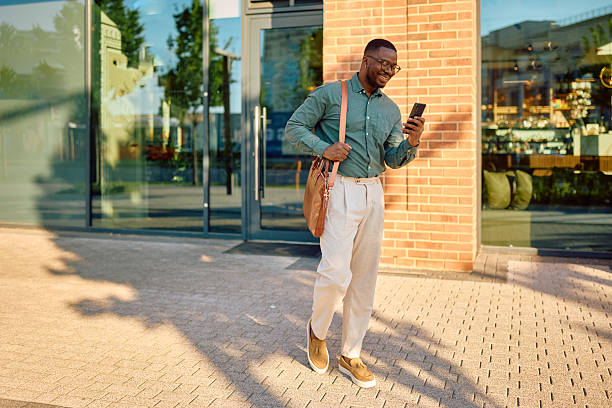 istock Smiling businessman walking and using smartphone in the city 2216125436