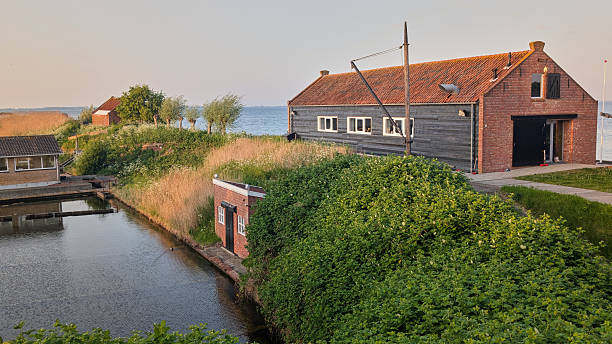 May 2, 2025 - Yerseke-Netherlands: Traditional oyster basins along the sea dike at sunset, with aquaculture work buildings and the calm Oosterschelde in the background.