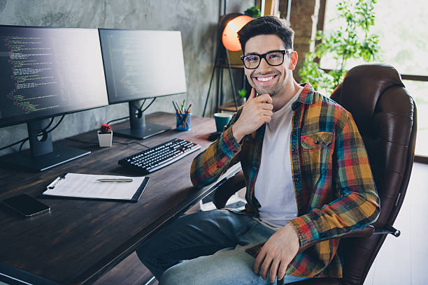 istock Photo young confident man think creative ideas touch chin in front of two pc monitors solving bugs program isolated indoors office 2216130779