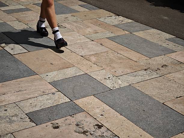 Woman with platform shoes and white socks walking on a patterned sidewalk made of beige and gray granite slabs