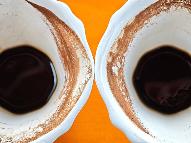 Two white cups with coffee leftovers forming a cinnamon ring are standing on an orange table, viewed from above