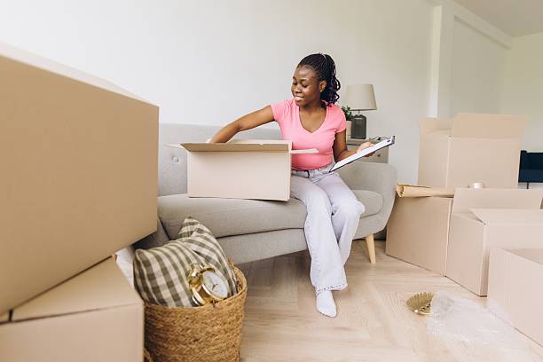 istock Young african american woman unpacking boxes and checking inventory list while moving into new apartment 2216135393
