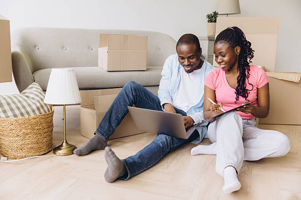 istock Young African American Couple Organizing Move Using Laptop and Checklist 2216135612