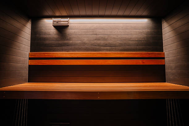 istock Modern sauna interior with dark wooden paneling, slatted bench seating, and overhead lighting, creating a serene, clean atmosphere. 2216138633