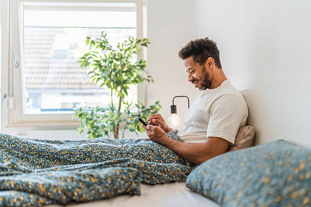 istock Black Male in Relaxed Setting Shopping Online Using Smartphone in Cozy Bedroom 2216149070