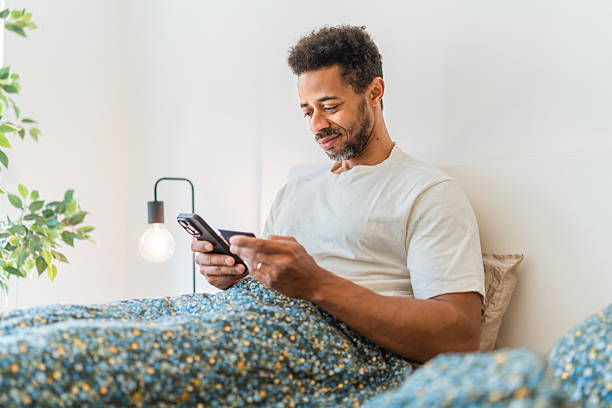 istock Mid Adult Black Man Relaxing in Bed Using Smartphone with Soft Natural Lighting 2216149098