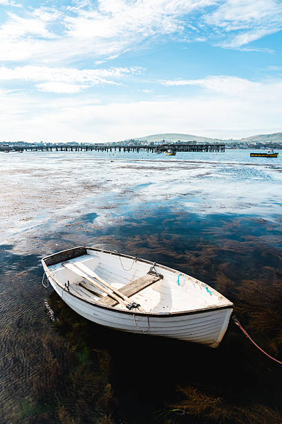 Peaceful scene of a white rowing boat moored in the shallow waters of swanage bay, dorset, uk, with a pier and distant hills in the background