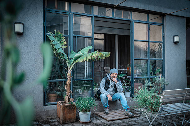 you man, propably a student, sitting on a stool in his backyard, spending his time thinking